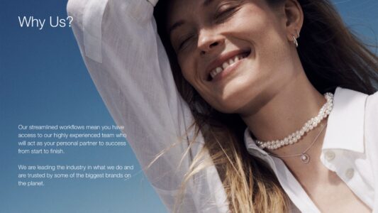 A person exudes joy, smiling under the blue sky, with eyes closed in delight. Wearing a white shirt, they accessorize with pearl necklaces and earrings. Sunlight glows on their skin, wind gently catching their long, flowing hair. Their head tilts back slightly, capturing a moment of pure contentment and freedom in a serene atmosphere.