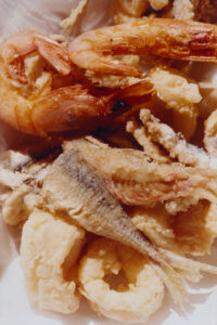 A delectable assortment of battered and fried seafood is presented, featuring a mix of golden shrimp, crispy calamari rings, and pieces of fish. The crispy texture is highlighted by the light, craggy coating. The seafood appears perfectly cooked, emitting a warm, inviting glow, promising a delightful blend of flavors and satisfying crunch with every bite.