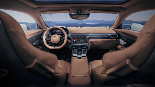 The interior showcases a luxurious cabin featuring tan leather seats, a sleek dashboard, and a modern steering wheel. The center console displays digital controls and a crisp screen. Large windows provide expansive visibility, while the panoramic roof adds openness. High-quality materials and elegant design elements combine for a sophisticated and comfortable driving environment, emphasizing technology and style.