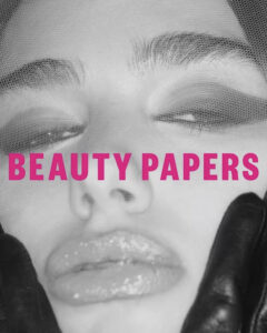 A close-up shot showcases a person's face with closed eyes and glossy lips, partially covered by a sheer, textured fabric. Dark, dramatic eyeshadow complements well-defined eyebrows. Black gloves gently touch the person's cheeks, adding a contrasting texture. The monochromatic color scheme enhances the artistic and bold aesthetic of the overall composition.