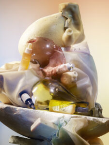 A collection of skincare products is artistically arranged on a textured, abstract surface. Various bottles and tubes, including serums and creams, are nestled among soft, flowing fabric-like forms and smooth, rounded objects. The scene is awash in warm, subtle lighting, creating a soothing and luxurious atmosphere with a blend of pastel and neutral tones.