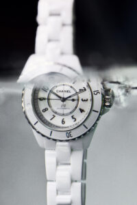 A sleek wristwatch is submerged in water, showcasing its water-resistant feature. The timepiece features a glossy white ceramic bracelet complemented by a striking round bezel. Its dial is adorned with bold, contrasting numerals and intricate watch hands. The setting captures a blend of elegance and functionality, emphasizing modern luxury and precision craftsmanship in a refined design.