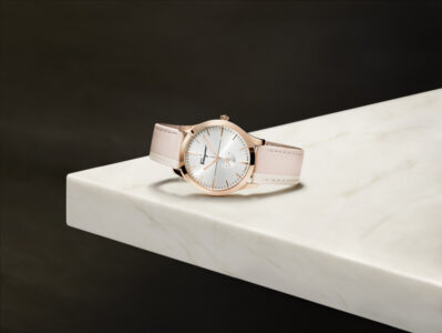 A sleek, elegant wristwatch rests on a marble surface. Its rose gold case encloses a silver dial, complemented by delicate gold hour markers. The blush pink leather strap adds a touch of sophistication, secured by fine stitching along the edges. The overall design exudes luxury and style, with a harmonious blend of subtle colors and refined materials.