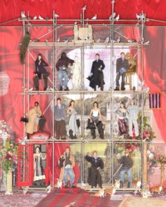 A theatrical scene with red curtains features models posing on a scaffold against a backdrop depicting classical architecture. Statues and pigeons adorn the setup, while various characters wear eclectic, fashion-forward clothing. A red phone booth and floral arrangements add vibrant accents. Corgi dogs roam below, enhancing the quirky and artistic atmosphere of this elaborate display.