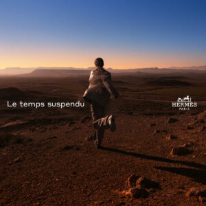 A person dressed in a suit is dynamically running across a rugged terrain during what appears to be sunset or sunrise. The sky transitions from deep blue at the top to warm oranges near the horizon, conveying a sense of freedom and exploration. The vast, barren landscape stretches into the distance with numerous hills and valleys visible.