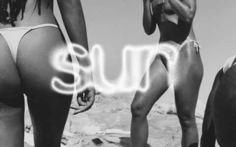 Three people stand outdoors wearing swimwear. The scene captures a sunny day with minimal clothing, highlighting relaxation and a carefree vibe. The composition focuses on the lower bodies and sand beneath them. The background features a clear sky, hinting at a warm, inviting atmosphere, typical of a beach or poolside setting, suggesting leisure and enjoyment.