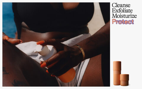 A person with bright orange nails and a gold bracelet applies lotion from an orange bottle onto their leg. They wear a black bikini top and have a tattoo. The setting suggests a sunlit environment near water. The focus is on skincare, emphasizing the routine of applying moisturizing products for protection and nourishment.