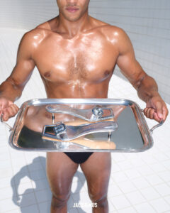A muscular individual wearing swimwear holds a large, shiny silver tray in a bright, tiled space. The tray features two metallic faucets placed on its surface. The scene is well-lit, highlighting the person's skin, with water creating a reflective effect. The composition is both striking and surreal, drawing contrast between the human form and industrial objects.