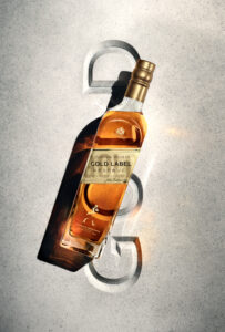 A tall, elegant bottle of amber liquid with a gold cap is set against a textured, light gray surface. The bottle casts a soft shadow, highlighting its sleek curves and transparency. Its golden hues contrast sharply with the cool background, creating a visual focus. Subtle lighting adds warmth, emphasizing the vibrancy and clarity of the contents.