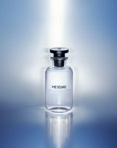 A sleek, transparent bottle stands centrally against a gradient background of soft blues and whites, creating an ethereal atmosphere. Light reflects off the bottle's smooth surface, highlighting its elegant curvature and the shiny, metallic black cap. The overall impression is one of sophistication and modern luxury, with a calming, almost celestial ambiance.