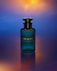 A sleek, dark glass bottle stands elegantly against a vibrant background blending rich orange, purple, and deep blue hues. The bottle features a cylindrical shape with a glossy, round cap on top. Light softly reflects off its surface, creating an aura of luxury and sophistication, while the surrounding colors enhance its allure and mystique.