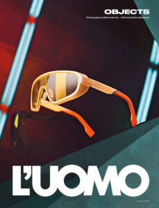 A pair of stylish sunglasses with orange-tinted frames and lenses is prominently displayed. The background features a series of futuristic, diagonal light bars in blue and red hues, creating a dynamic, modern aesthetic. The overall composition focuses on showcasing the sunglasses as a fashion accessory, emphasizing their vibrant colors and contemporary design.