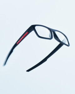Sleek black eyewear featuring a modern square frame design is angled against a light background. A red stripe adds a touch of color on the side, enhancing the contemporary look. The minimalist and lightweight build underscores elegance and functionality. Designed for a blend of style and comfort, it embodies a fashionable yet practical accessory.