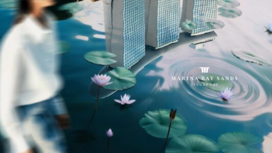 A serene scene features a blurred person in the foreground with water lilies and lily pads. Behind them, three modern towers with a unique design are reflected in the water, creating a harmonious blend of nature and architecture. Soft ripples spread across the water, adding a sense of tranquility to the composition.