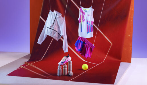 A stylish sports setup features a white and pink athletic outfit suspended above a backdrop with geometric designs. A matching sneaker rests on cylindrical stands, paired with a tennis ball for a dynamic touch. The scene is framed by vibrant red and orange hues, creating a modern, lively atmosphere perfect for athletic enthusiasts.