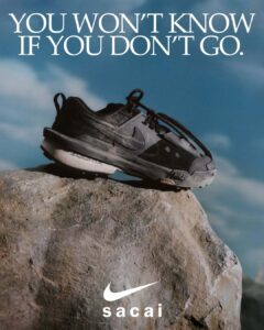 A single black sneaker is placed on a rugged rock, with its design featuring multiple layers and visible branding. The shoe's textured sole hints at its durability and traction. A vast blue sky with soft clouds forms the background, enhancing the sense of adventure and exploration. Shadows on the rock highlight its uneven surface, adding depth.