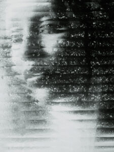A barely visible face emerges through a wet, textured surface, illuminated by soft light. The scene is abstract, evoking a sense of mystery and introspection. The combination of shadows and highlights creates a monochromatic, dreamlike atmosphere. Drops of moisture distort the features, adding an element of depth and obscurity to the serene, contemplative expression.