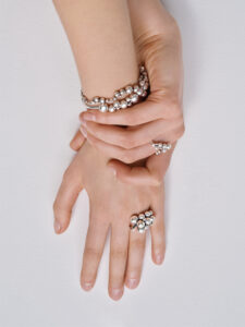 Two hands display elegant jewelry adorned with clusters of pearls. A bracelet wraps around one wrist, and a matching ring graces a finger. The pose showcases the jewelry, emphasizing the shimmering pearls. The smooth, pale skin of the hands contrasts with the intricate, luminous design of the accessories, creating a sophisticated and delicate aesthetic.