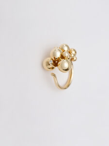A sleek gold ring features a cluster of shiny, spherical beads, creating an elegant and contemporary design. Several gleaming orbs vary in size and are closely grouped together atop the ring, catching light beautifully. The composition exudes sophistication with its minimalist style, ideal for adding a touch of modern elegance to any ensemble.