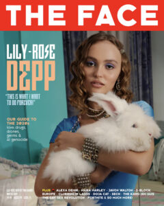 A person with wavy, light brown hair holds a fluffy white rabbit. The individual wears a blue outfit accessorized with a gold chain and dangling earrings. Their makeup includes blue eyeshadow. The background features a curtain and a turquoise wall. The composition is stylish and carefully arranged, suggesting a fashion-oriented aesthetic with a focus on elegance and poise.