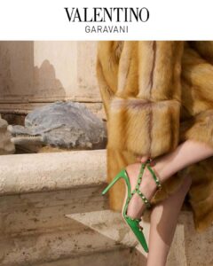 A luxurious scene showcases a person draped in a rich brown fur coat, elegantly seated against an ornate stone backdrop. Their legs are highlighted by vibrant green high heels adorned with gold studs. The sophisticated ensemble contrasts against the textured, weathered stone architectural elements, adding an opulent touch to the classic setting.