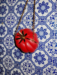 A vibrant composition features a red, intricately designed object resembling a flower, suspended by a gold chain. It is set against a background of ornate blue and white tiles, each adorned with symmetrical floral patterns. The vivid contrast between the red and the cooler-toned tiles creates a striking visual effect, highlighting the artistry and detail.